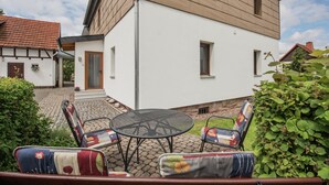 A house with a white exterior and wooden siding, a paved courtyard, and outdoor furniture. - Charming Home in Winterstein (Waltershausen)