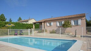 Ein Schwimmbad mit weißem Zaun, einer überdachten Terrasse und einem Haus im Hintergrund.