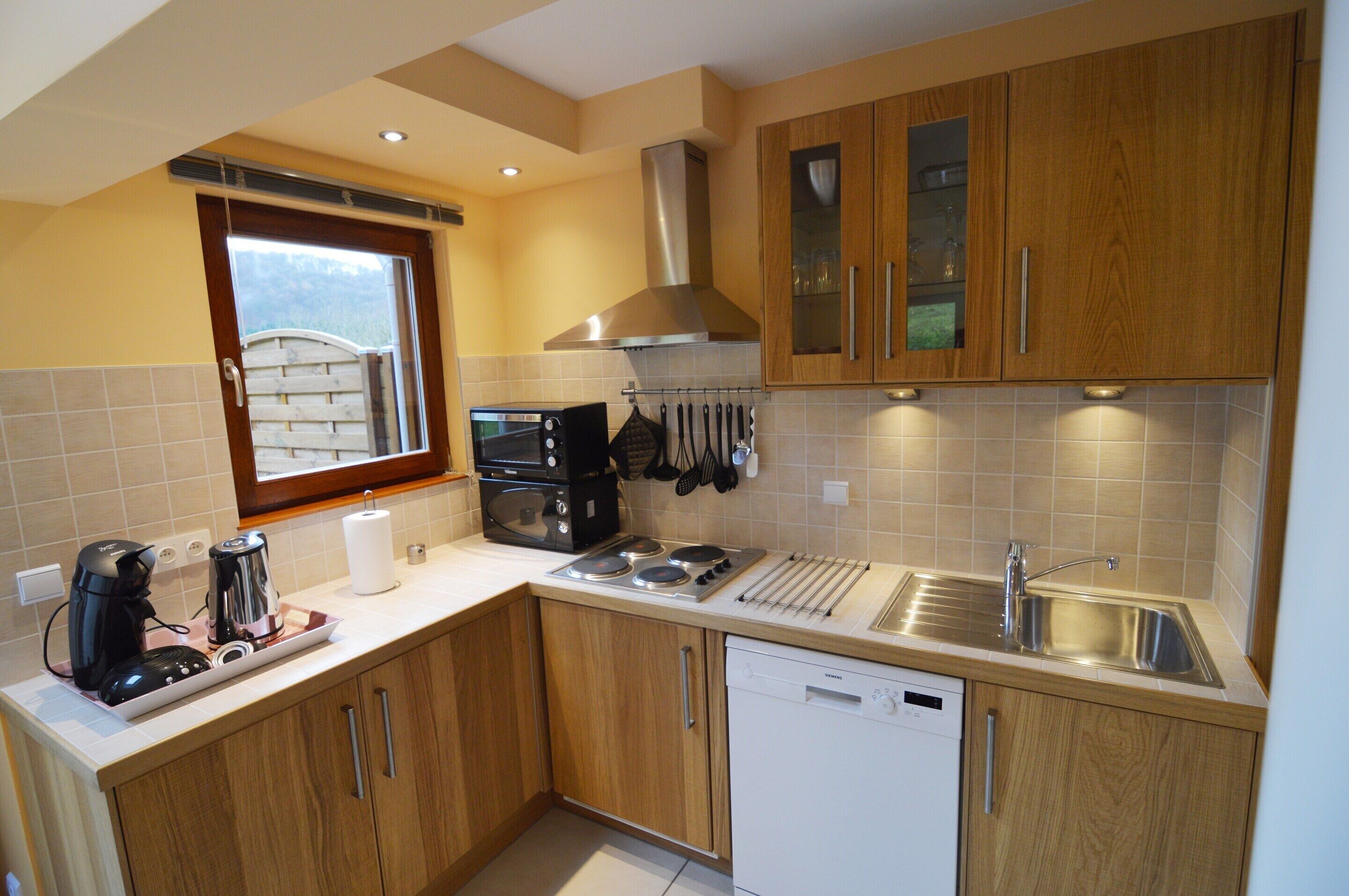 A modern kitchen with wooden cabinets, a built-in oven, a coffee maker, and a dishwasher.