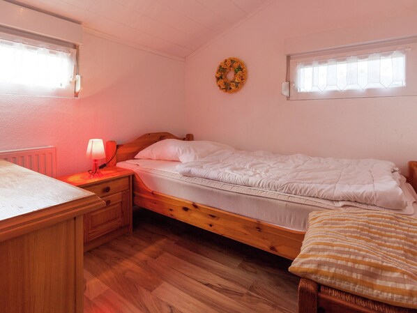 A single bed with a wooden frame, a bedside table with a lamp, and a window with a white blind.