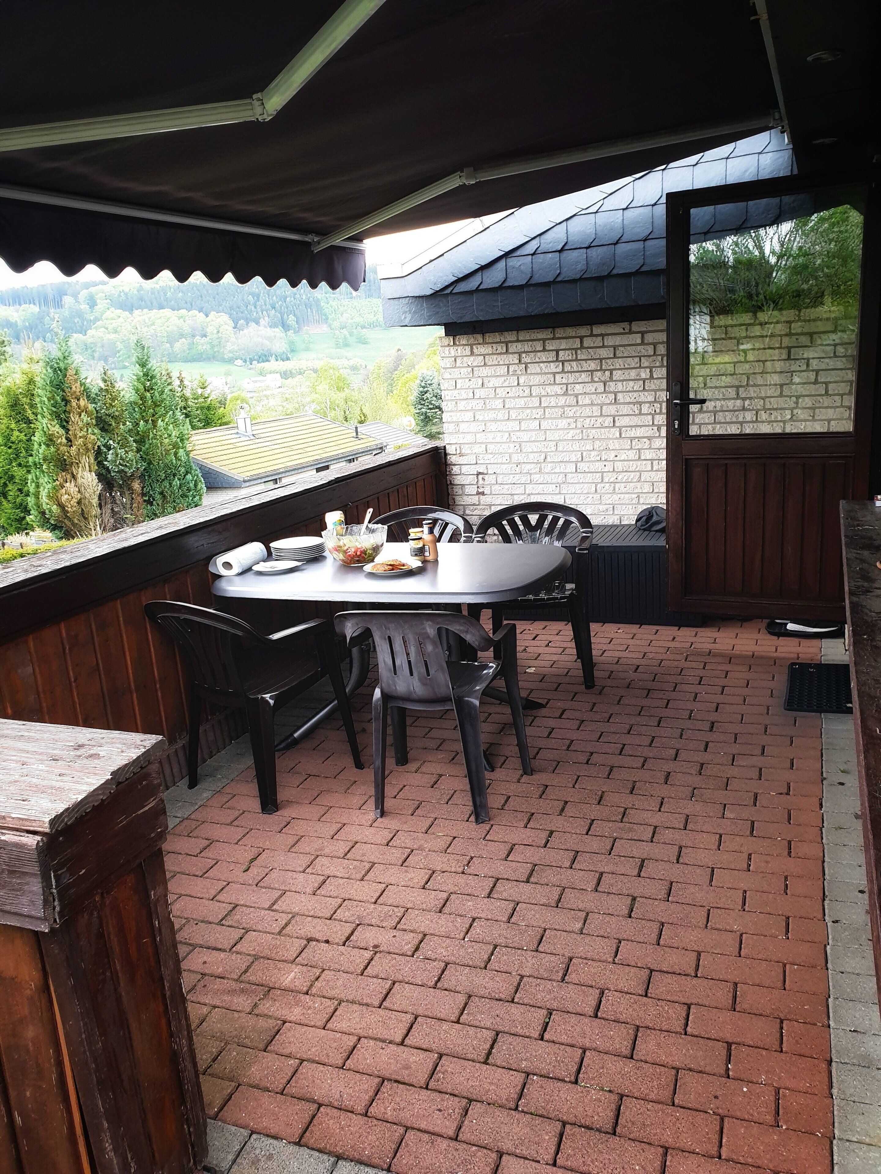 A covered patio with a brick floor, a round table, and chairs.