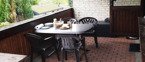 A covered patio with a brick floor, a round table, and chairs.