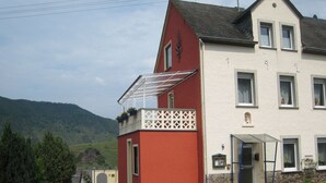 A two-story building with a red and white facade, a balcony with potted plants, and a view of a hilly landscape. - Holiday Home in the Eifel With Balcony (Bremm)