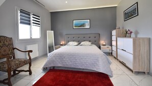 Une chambre à coucher comprenant un lit, une chaise, une table de chevet, une commode, un radiateur et un tableau accroché au mur.