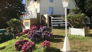 Une maison à deux étages dotée d’un balcon, entourée de jardins bien entretenus et d’une clôture blanche.
