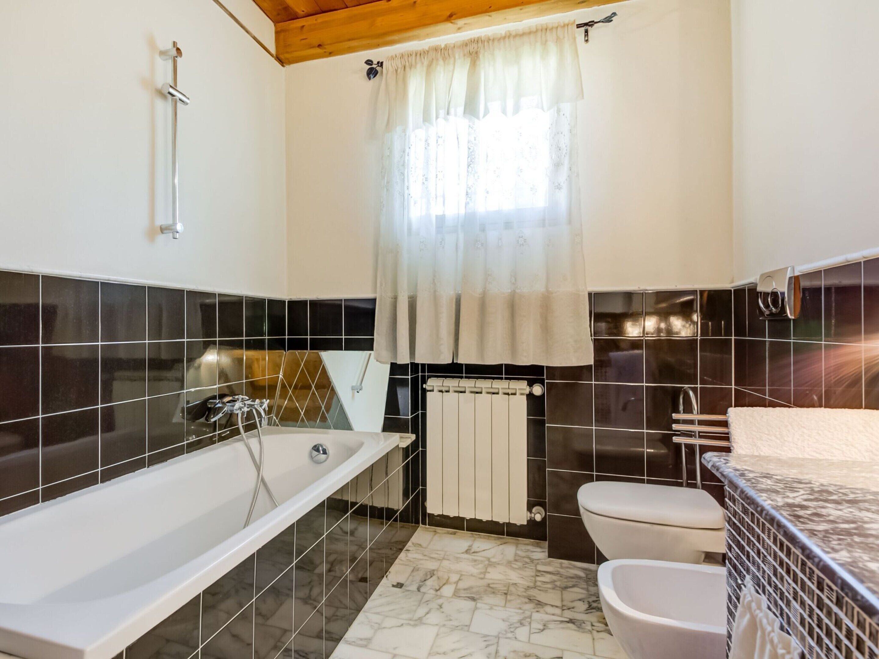 Une salle de bain avec une baignoire, des toilettes et une fenêtre avec un rideau.