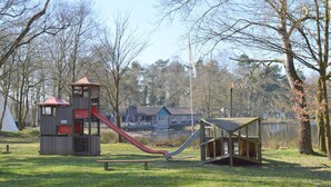 A playground with a slide and climbing structures, surrounded by trees and a lake.