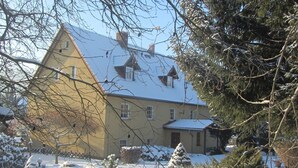 Une maison à deux étages, dont le toit est recouvert de neige, et qui est précédée d’un jardin.