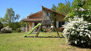 A house with a swing set, a slide, and a garden with white flowering bushes. - Relaxing Retreat in Bathernay (Bathernay)