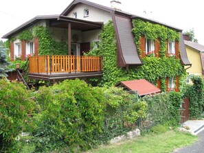 A two-story house with a wooden deck, a small porch, and a red-roofed shed.