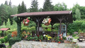A wooden gazebo with a stone base, surrounded by potted plants and flowers. - Modern Apartment in Carlsbad With Garden (Karlovy Vary)