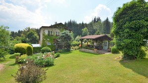 A well-maintained garden with a gazebo, a house with a sloped roof, and a variety of shrubs and flowers. - Modern Apartment in Carlsbad With Garden (Karlovy Vary)