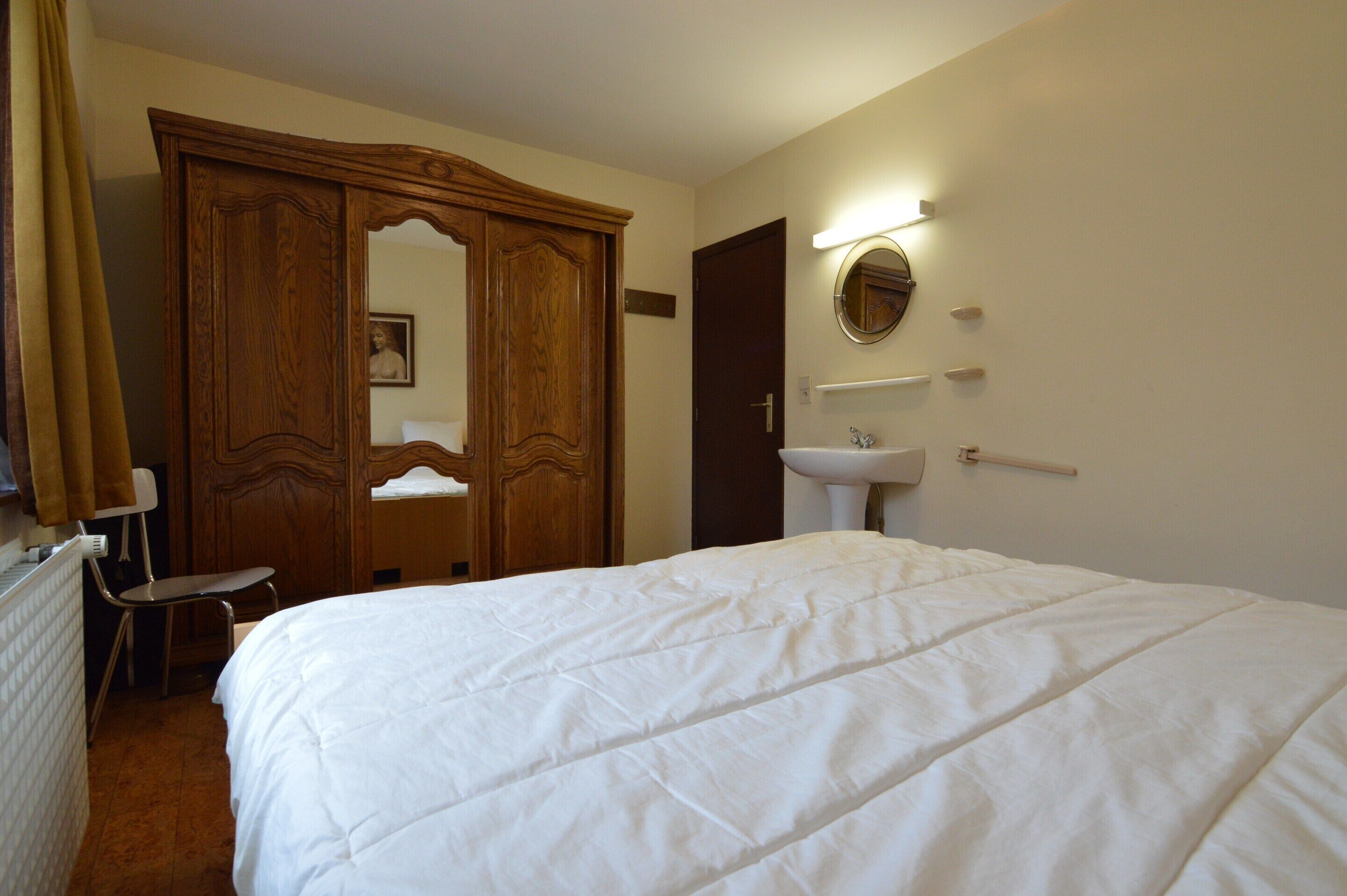 A hotel room with a large bed, a wooden wardrobe, a mirror, and a white sink.