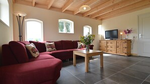Ein Wohnzimmer mit einem roten Ecksofa, einem Holztisch, einem Fernseher auf einem Schrank und einem großen Fenster.