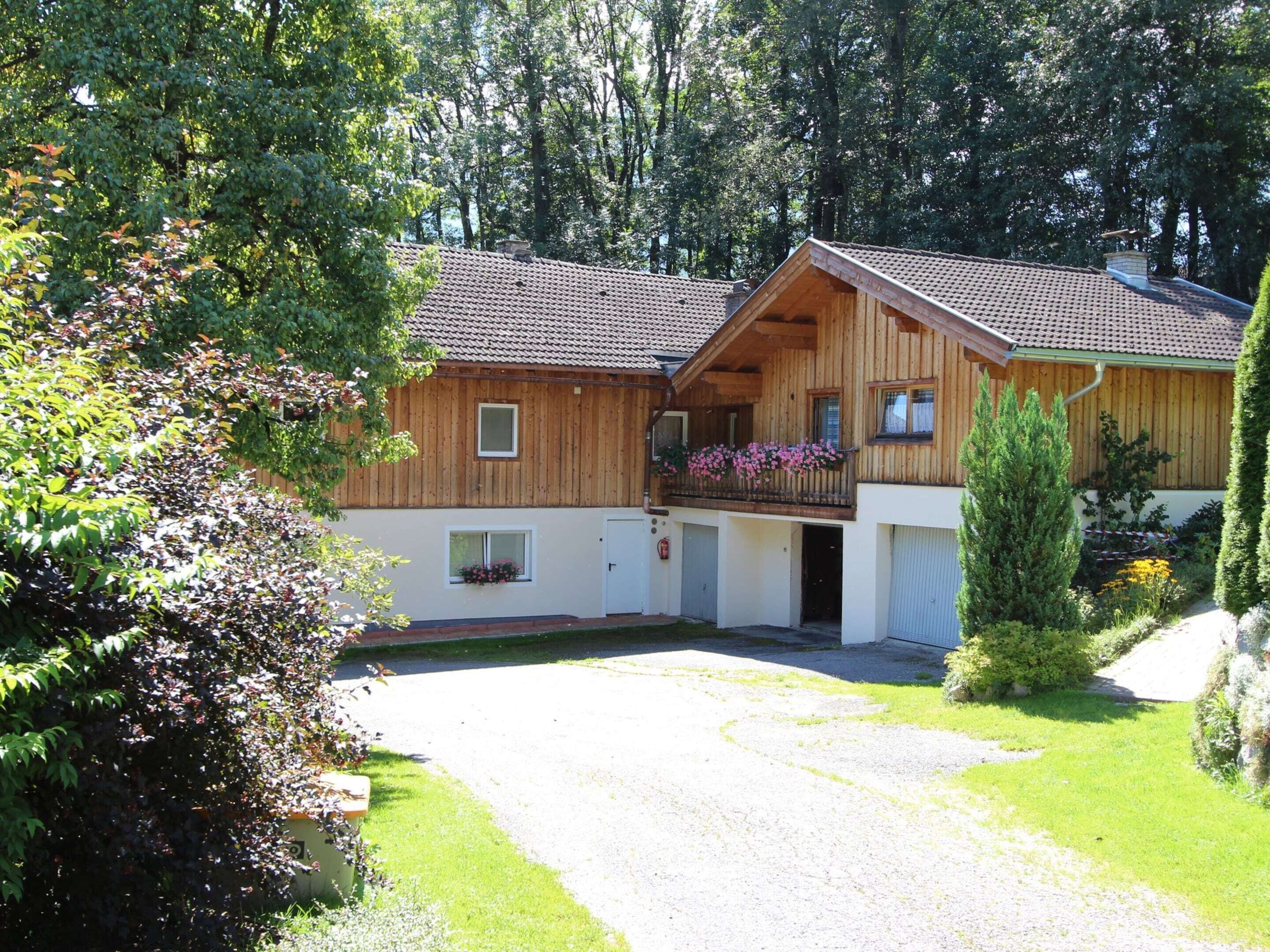 A two-story wooden building with a balcony, surrounded by greenery and trees.