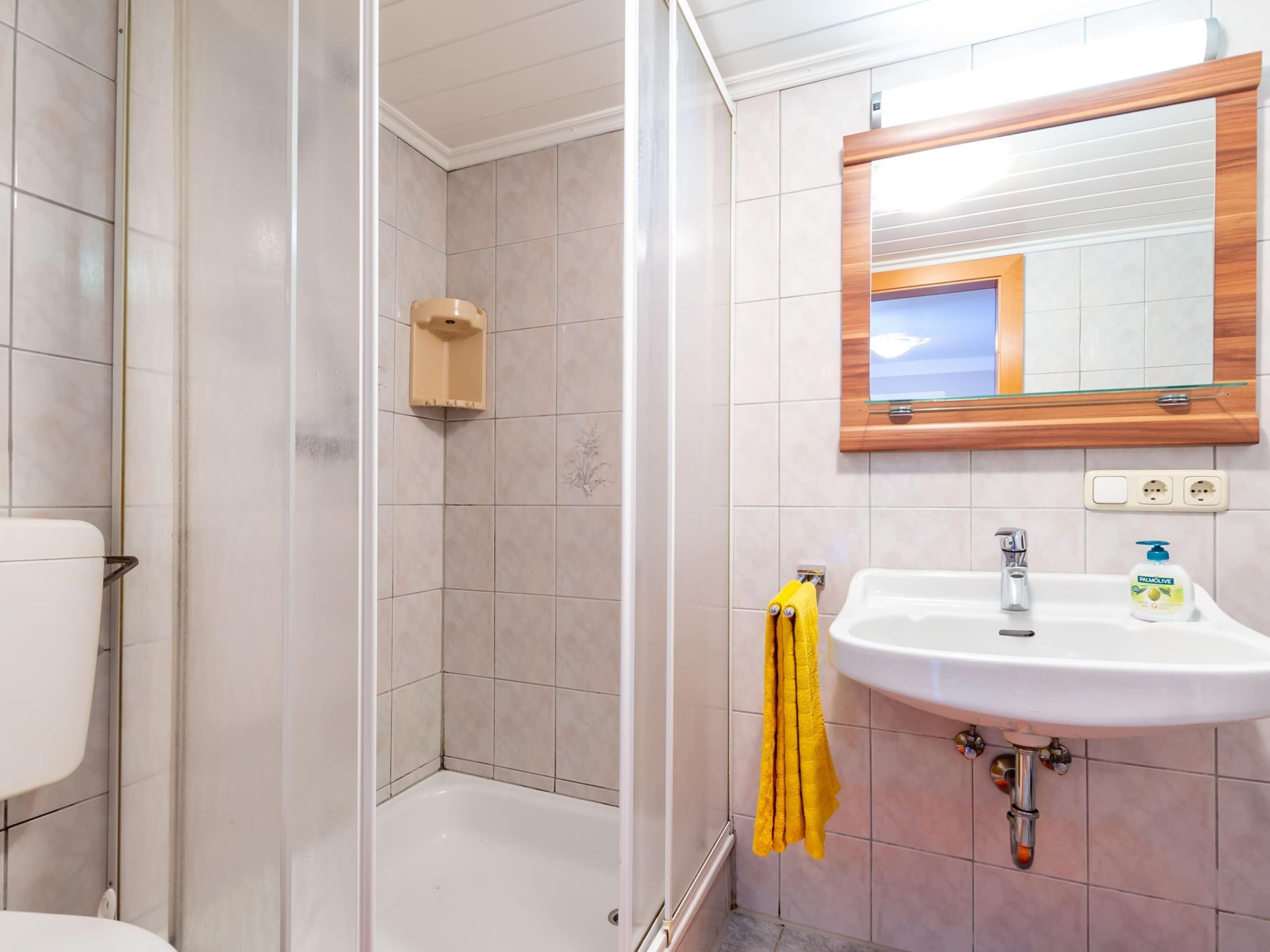A bathroom with a shower, toilet, sink, and mirror.