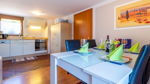 A modern kitchen with white cabinets, a built-in oven, and a microwave. There is a dining table with chairs and a painting on the wall. - Simplistic Apartment in Piesendorf - Walchen near Ski Slopes (Piesendorf)