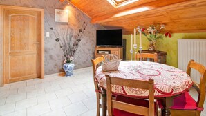 Un coin repas accueillant avec un plafond en bois, une lucarne, une table à manger entourée de chaises, un vase de fleurs et un téléviseur en arrière-plan.