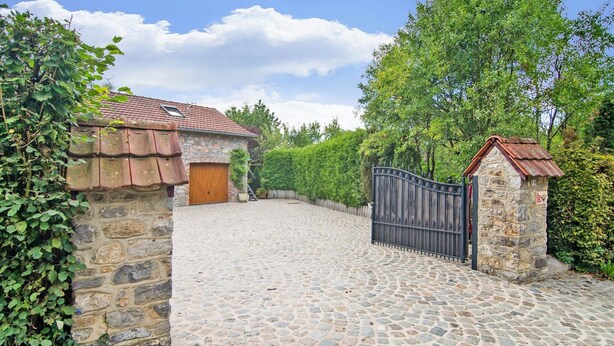 Une allée pavée de pierres menant à un bâtiment en pierre doté d’une porte en bois et d’un portail en métal.