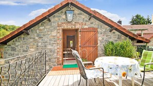 Une petite maison en pierre avec une porte en bois, un petit porche doté d’une table et de chaises, et une rambarde en métal.