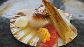 Un dessert présenté dans une assiette, avec une coquille de Saint-Jacques comme base, un élément rond de couleur blanche, un morceau de fruit et une tranche de fruit caramélisé.