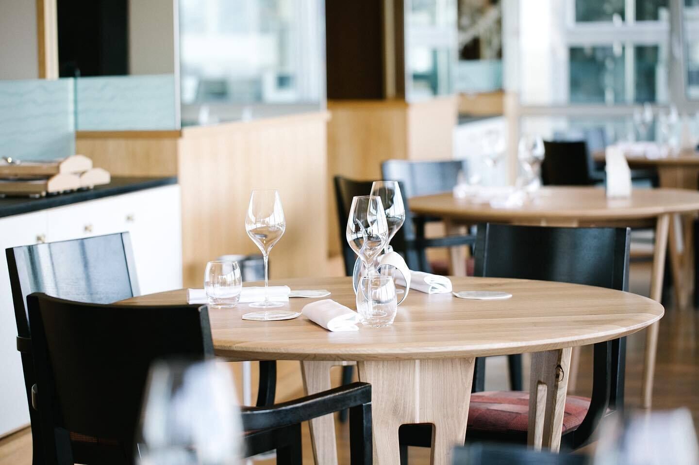 A dining area with round tables, chairs, and wine glasses.