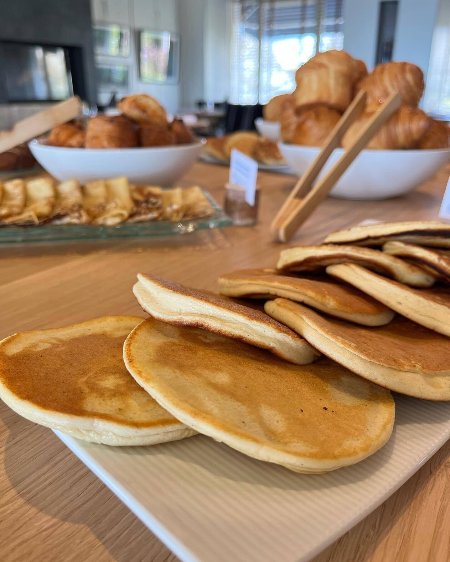 A breakfast buffet with pancakes, croissants, and other pastries on a wooden table.