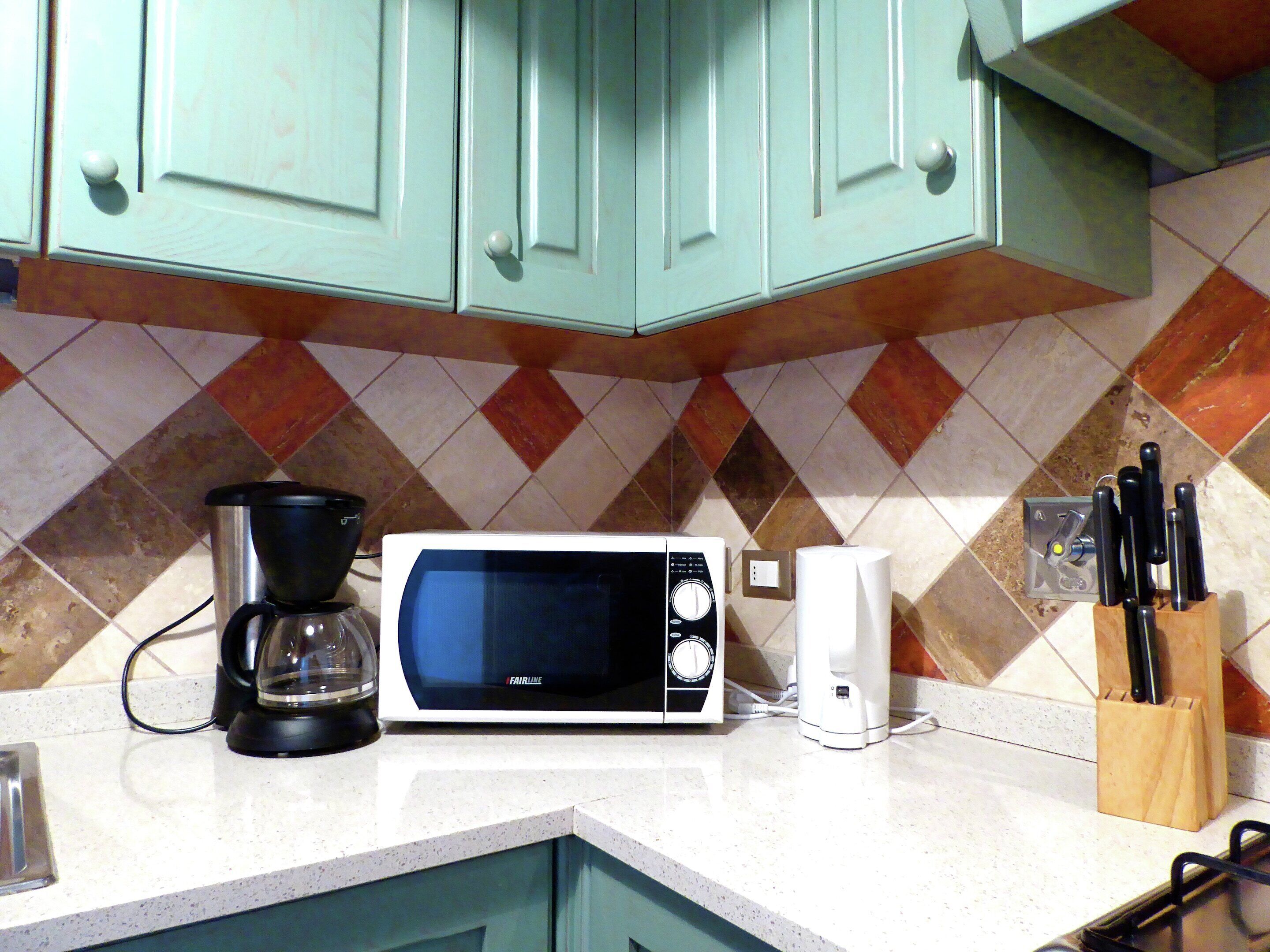 A kitchen with teal cabinets, a microwave, a coffee maker, and a knife block.