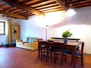 A dining area with a wooden table and chairs, a vase with flowers, a sofa, and a window with curtains. - Holiday Home in Montecarelli With Pool (Barberino di Mugello)