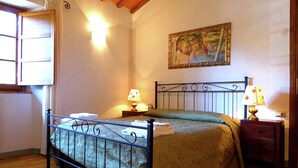 Um quarto com estrutura de cama de metal, duas mesas de cabeceira com luminárias, um quadro na parede e uma janela com cortinas.