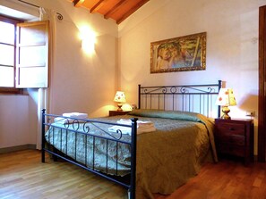 Une chambre Ă coucher avec un lit en mĂ©tal, deux tables de chevet avec des lampes, un tableau au mur et une fenĂȘtre avec des rideaux.