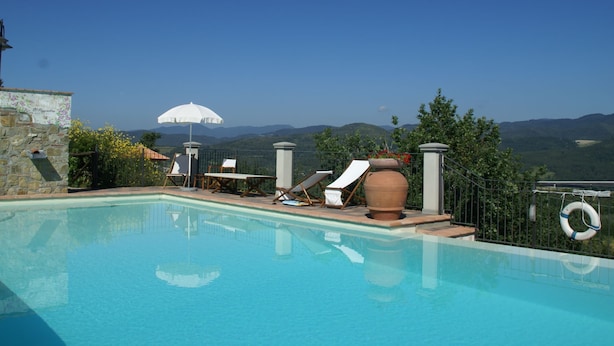 Piscina azul clara com espreguiçadeiras e um grande vaso de terracota.