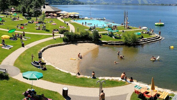 Ein Seehotel mit Schwimmbad, Liegestühlen und einer Rasenfläche.
