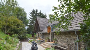 A stone building with a sloped roof, surrounded by a garden with various plants and a statue. - Cozy Apartment in Immerath near Fishing (Immerath)