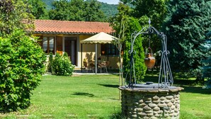 A stone well with a metal structure, surrounded by lush greenery and a house with a tiled roof in the background. - Beautiful Farmhouse With Pool (San Marcello Piteglio)