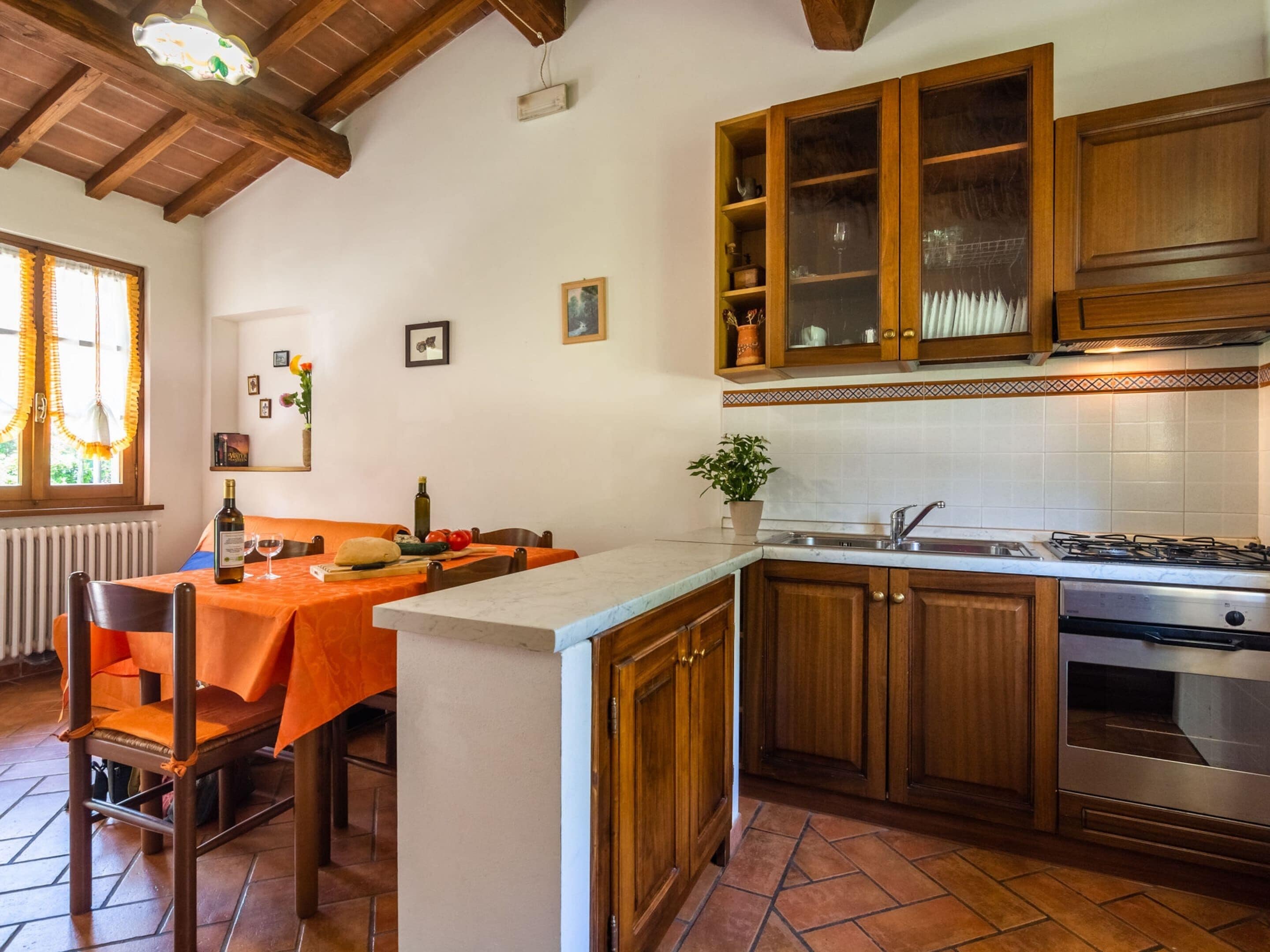 Una cucina con mobili in legno, zoccolo schienale piastrellato e zona pranzo con tavolo apparecchiato per due.