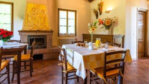 A dining area with a fireplace, a table set for breakfast, and a large painting on the wall. - Beautiful Farmhouse With Pool (San Marcello Piteglio)