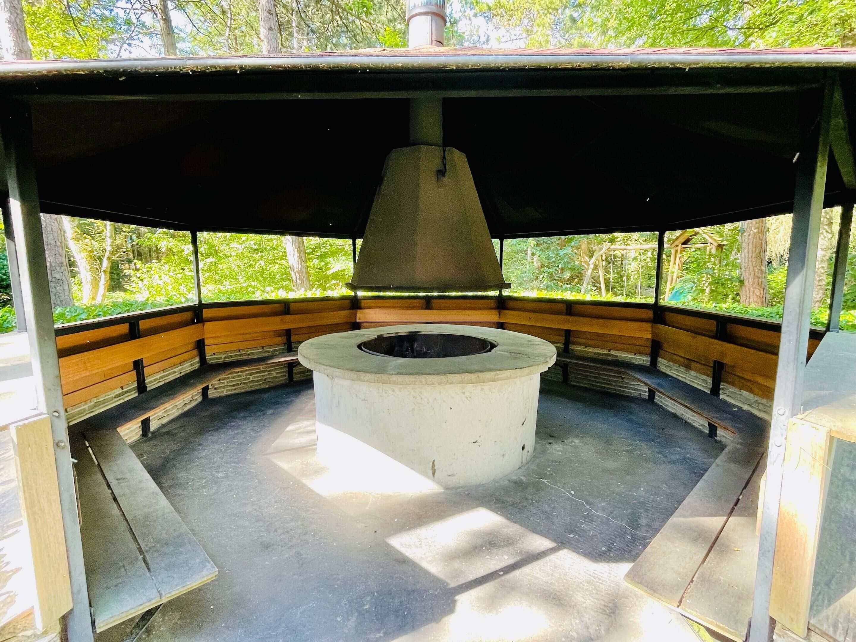 Un área de estar al aire libre cubierta con bancos y una chimenea central.