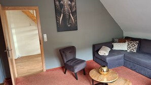 A living room with a grey sofa, a grey armchair, a small round table with a decorative object, and a large elephant artwork on the wall. - Apartment Near Willingen With Terrace (Willingen)