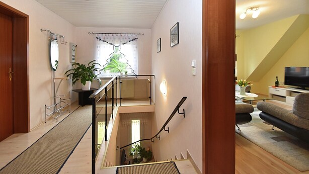 Ein mehrgeschossiges Wohnzimmer mit Treppe, einer Couch und einem Fernseher.