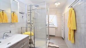 Ein modernes Badezimmer mit Duschkabine aus Glas, einem weißen Waschbecken und einem gelben Handtuchhalter.