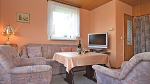 A cozy living room with a wooden ceiling, a sofa, two armchairs, a table with a bottle and glasses, a television, and a window with curtains. - Cozy Holiday Home in Großbreitenbach near Schwarza Valley (Grossbreitenbach)