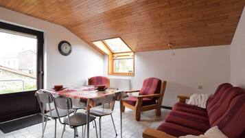 Una habitación acogedora con techo de madera, una mesa de comedor con sillas, un sofá y un ventanal con vistas al exterior.