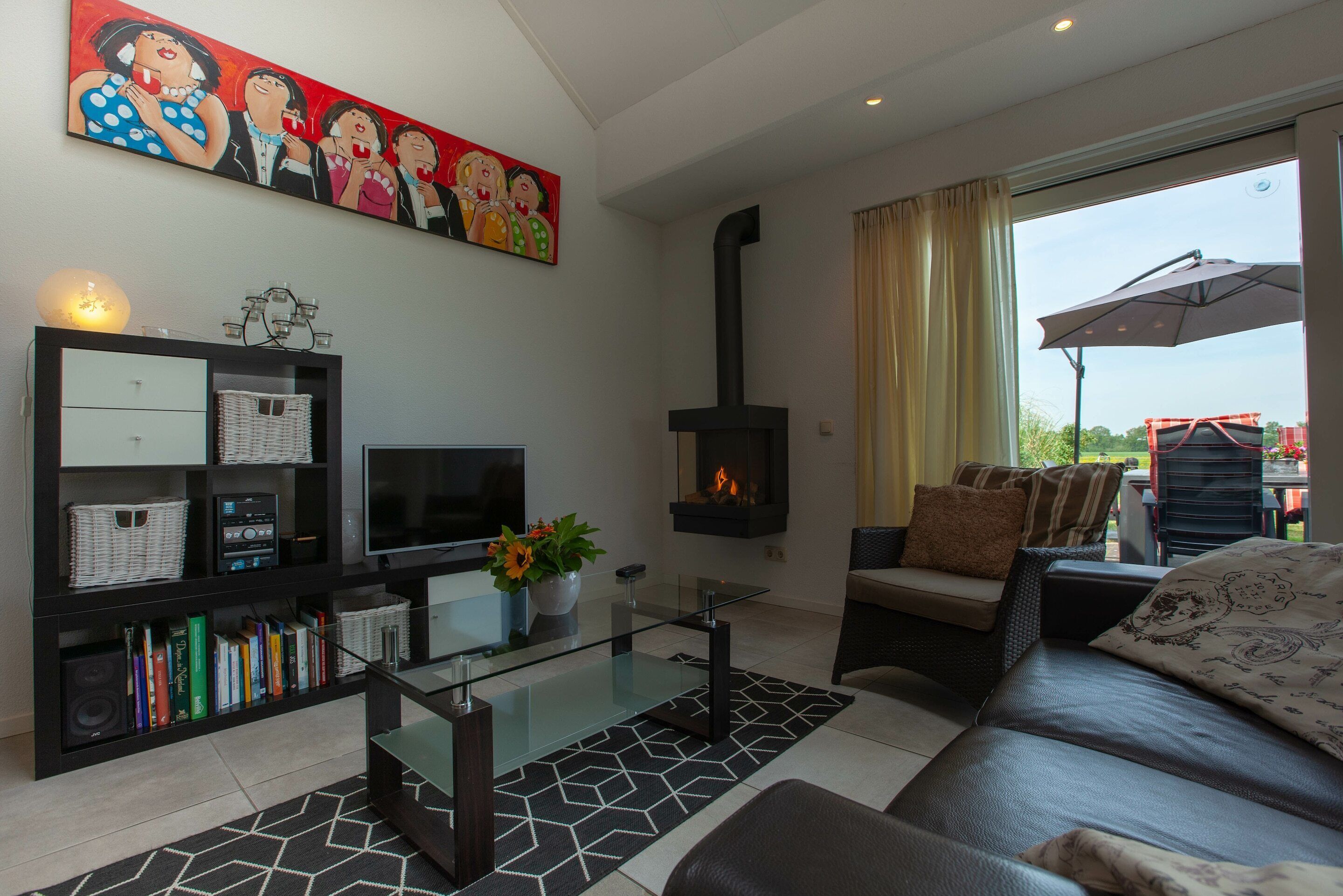 A living room with a fireplace, sofa, TV, bookshelf, and a large window with curtains.