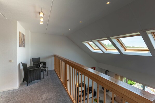 A spacious room with a high ceiling, skylights, a wooden railing, and a seating area with a table and chairs. - Holiday Home With Private Terrace (Langweer)