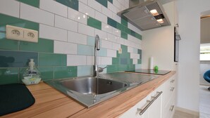 Eine moderne Küche mit Spüle aus Edelstahl, einer Holzarbeitsplatte und einer Spritzschutzleiste mit grünen und weißen Fliesen.