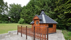 Eine Holzhütte mit geneigtem Dach und Schornstein, umgeben von einem Holzzaun und einem Kiesweg.