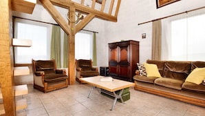 A living room with a wooden ceiling, two armchairs, a sofa, a cabinet, and a table. - Holiday Home in Peaceful Setting and Large Garden (Rendeux)