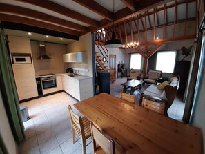 A modern kitchen with built-in appliances, a dining area with a wooden table and chairs, and a staircase leading to another level. - Holiday Home in Peaceful Setting and Large Garden (Rendeux)