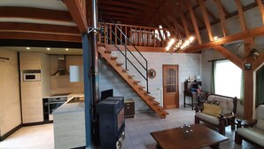 A spacious living area with a wooden staircase, a kitchen with modern appliances, and a cozy seating arrangement. - Holiday Home in Peaceful Setting and Large Garden (Rendeux)